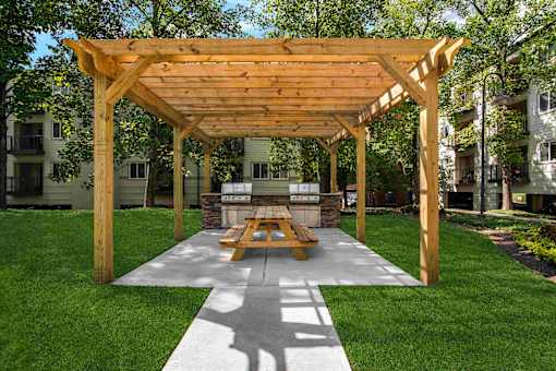 A wooden pavilion with a picnic table in the middle of a grassy area.