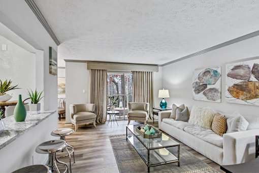 A living room with a white couch, a glass coffee table, and a large window with curtains.