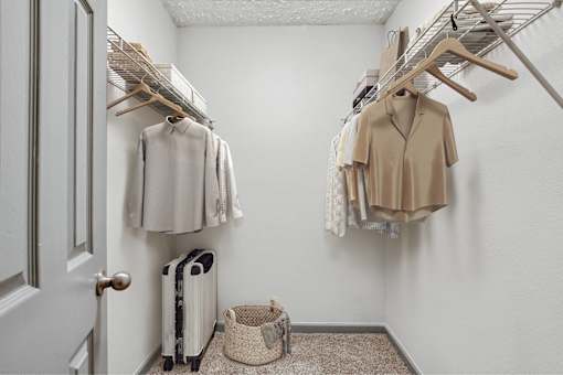 A white closet with clothes hanging and a basket on the floor.