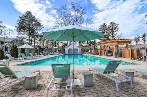 A pool with a green umbrella and chairs around it.