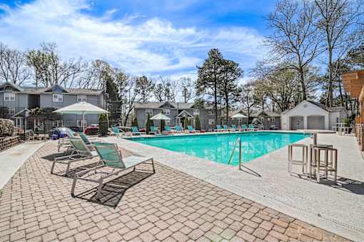 A pool surrounded by chairs and trees.