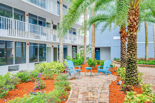 a courtyard with palm trees and chairs in front of a building