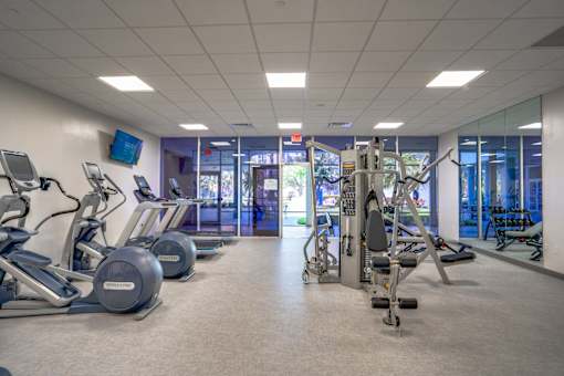 a gym with cardio equipment and weights in a building with glass doors
