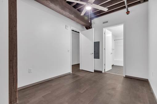 A room with a wooden floor and white walls with a ceiling fan.