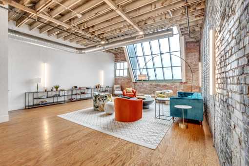A room with a brick wall and wooden floors has a large window and a variety of seating options.