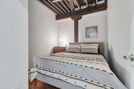 A bed with a wooden frame and a striped comforter is in a room with white walls.