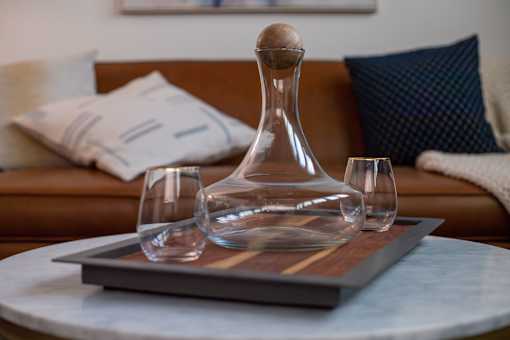 A decanter and two glasses are placed on a wooden tray on a round table.