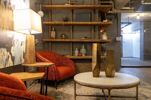 A room with a red couch, a round table, and a shelf with various objects on it.