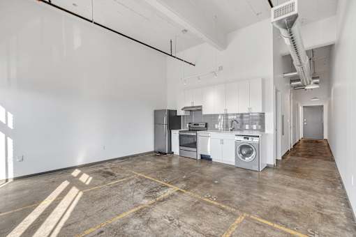 A large empty room with a kitchenette and a washer and dryer.