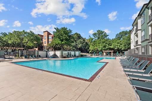 A large outdoor swimming pool surrounded by lounge chairs and trees.