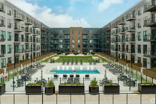 A large pool surrounded by lounge chairs and planters is surrounded by apartment buildings.