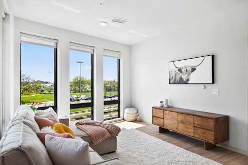 A living room with a couch, a painting of a cow, and a large window.