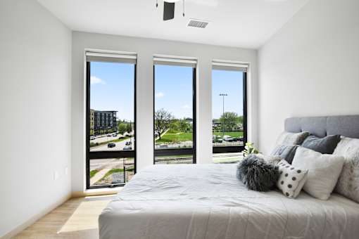 A bedroom with a large bed and a view of the outside through the windows.