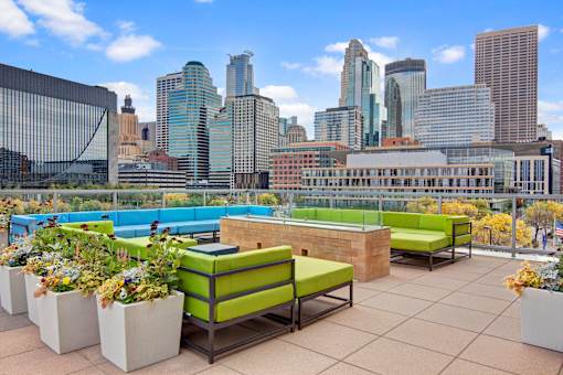 A rooftop patio with green seating and a view of a city skyline.