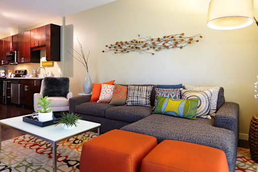 A living room with a grey couch and orange ottoman.