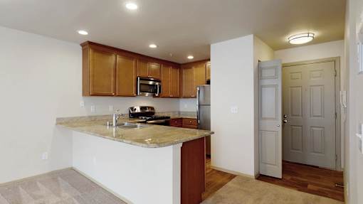 A bright kitchen here at Windsong featuring warm wood cabinetry, spacious breakfast bar, and sleek stainless steel appliances. Neutral finishes and open layout create an inviting, functional space perfect for cooking and entertaining.
