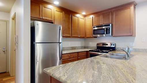 A bright kitchen here at Windsong featuring warm wood cabinetry, sleek stainless steel appliances, and spacious granite countertops. Clean finishes and efficient layout create a welcoming, functional space ideal for everyday cooking and dining.