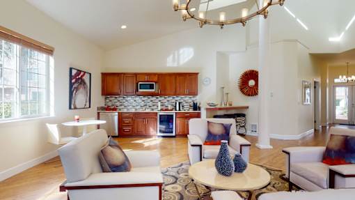 A resident lounge here at Windsong featuring cozy armchairs, a round coffee table, and a kitchenette with warm wood cabinets. Bright and welcoming, this stylish space offers high ceilings, large windows, and comfortable seating perfect for relaxing or socializing.