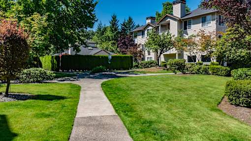 A landscaped outdoor courtyard here at Windsong featuring a lush green lawn, mature trees, and a peaceful walking path. This bright and welcoming space offers scenic greenery and a relaxing setting perfect for enjoying fresh air.