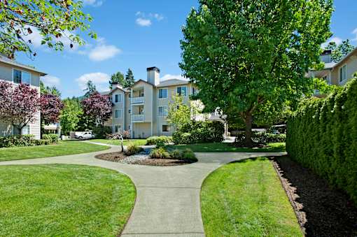 A landscaped courtyard here at Windsong featuring lush green lawns, curved walking paths, and mature trees. This bright and inviting outdoor space offers scenic surroundings, well-maintained greenery, and a peaceful setting for relaxing strolls.