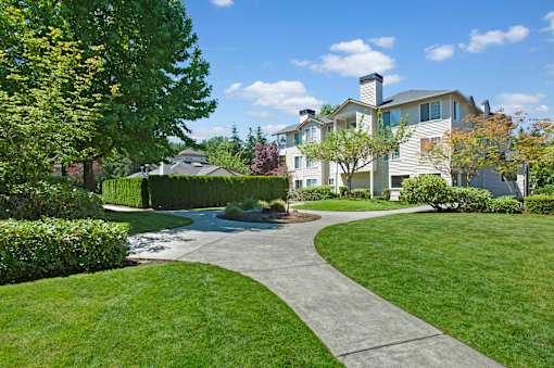 A landscaped outdoor courtyard here at Windsong featuring green lawns, curved walking paths, and mature trees. This bright and inviting setting offers peaceful surroundings, well-maintained greenery, and a pleasant space for relaxing strolls outdoors.