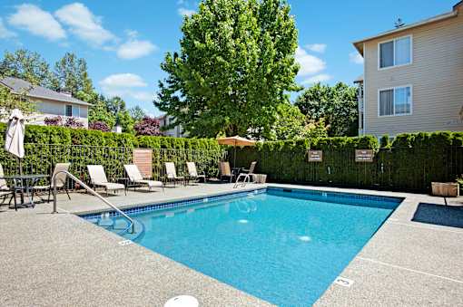 A refreshing outdoor pool here at Windsong surrounded by lush greenery and charming apartment buildings. This bright and inviting space features clear blue water, comfortable lounge chairs, and a peaceful atmosphere perfect for relaxing on sunny days.