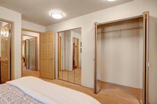 A bright bedroom closet area here at Windsong featuring spacious mirrored sliding doors and ample storage. Clean, open layout with soft carpet and convenient access to the adjoining bedroom and bathroom areas.