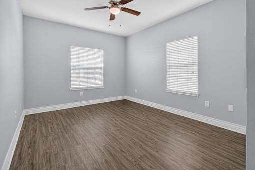 A room with a ceiling fan and two windows with blinds.