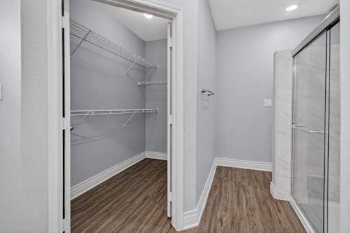 A walk-in closet with white shelves and a glass door.