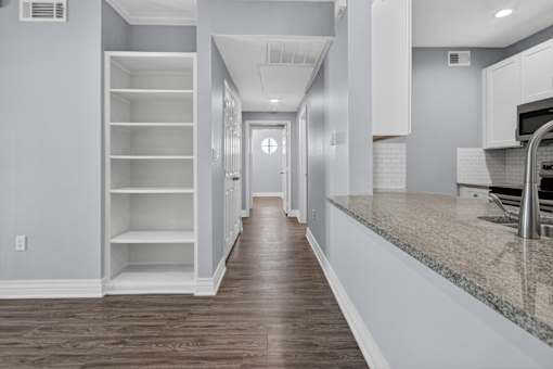 A long hallway with a door at the end and a kitchen area on the right.