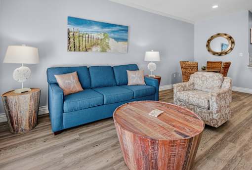 A living room with a blue couch, two lamps, a wooden coffee table, and a painting on the wall.