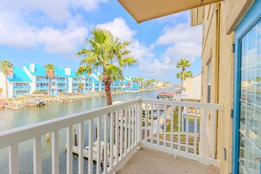 A balcony overlooks a body of water with a palm tree in the distance.