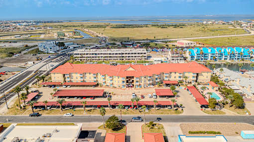 A large building with a red roof is surrounded by a parking lot and palm trees.