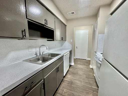 Modern kitchen at Greenbriar Place 55+ Apartments in Corpus Christi featuring white cabinets, stainless steel sink, and full-size refrigerator.
