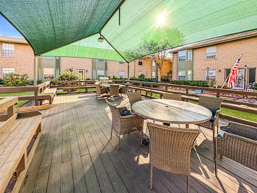 A wooden deck with a table and chairs under a green canopy.