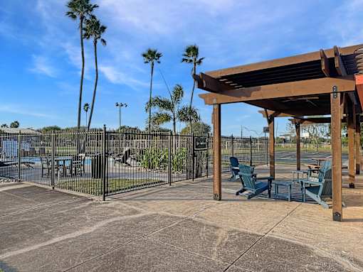 A wooden pergola is in the middle of a patio with chairs and a table.