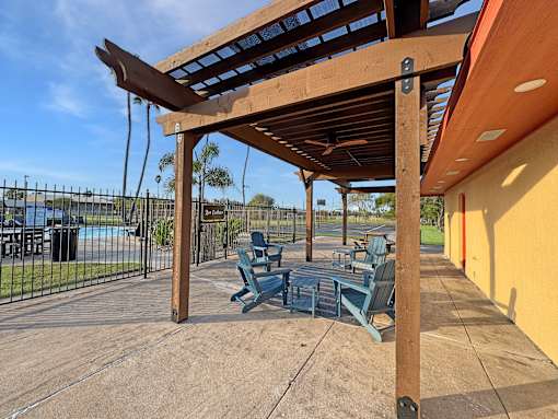 A wooden pergola with blue benches is in the foreground of a sunny day.