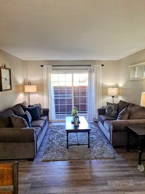 A living room with two couches, a coffee table, and a window at Raintree Apartments, CA 92346