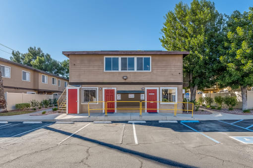 a small brown building with red doors and yellow railing in front of a parking lot