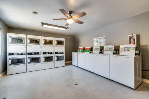 a laundry room with white washers and dryers and a ceiling fan