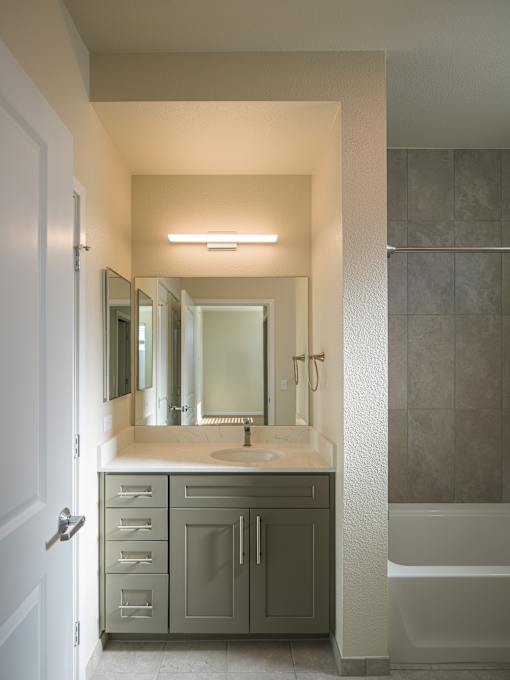 A bathroom with a sink, mirror, and bathtub.