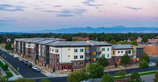 A street view of a residential area with apartment buildings and cars parked on the side of the road.