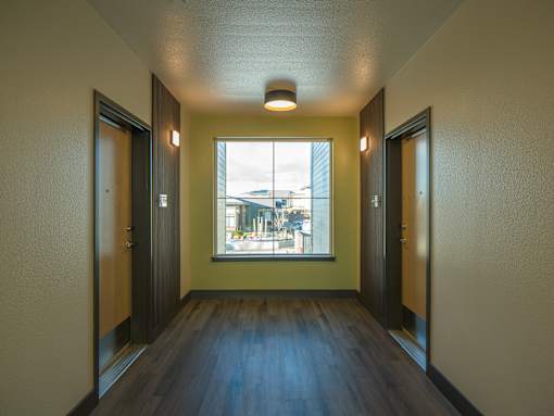 A long hallway with doors on both sides and a window in the middle.