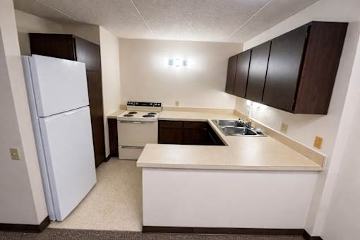 A small kitchen with a white refrigerator and brown cabinets.