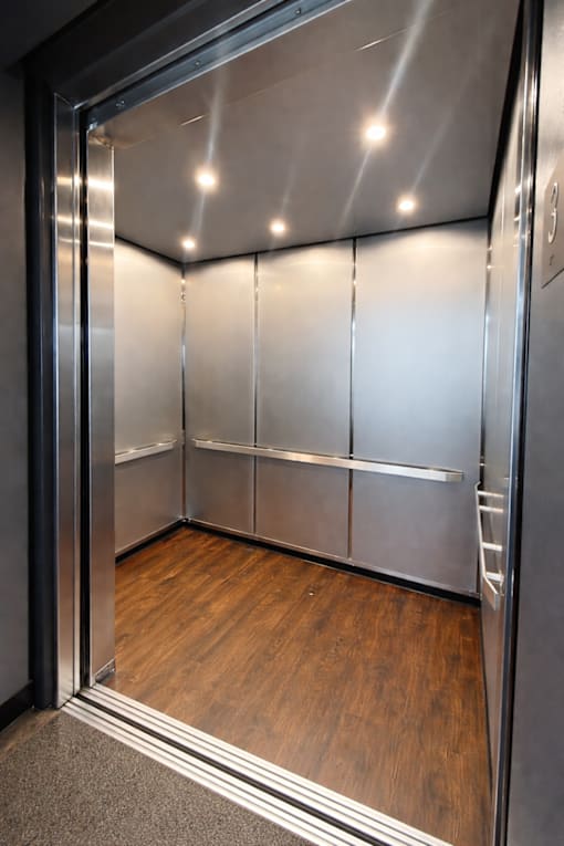 A stainless steel elevator with a glass door and wood flooring inside.