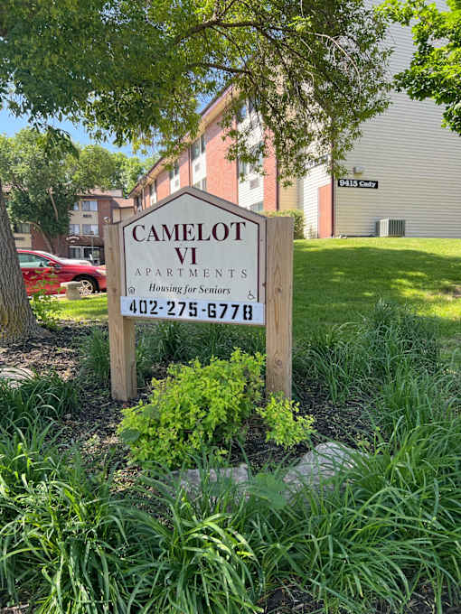 A sign for Camelot Apartments is in front of a building.