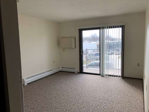 A room with a carpeted floor, a window with blinds, and a sliding glass door.