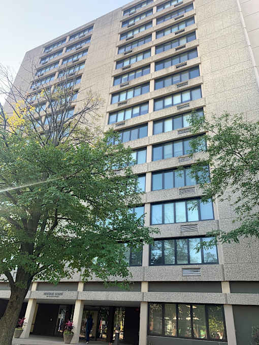 A tall building with many windows and a tree in front.