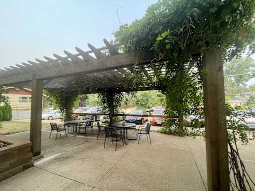 A wooden pergola with green vines growing on it is situated over a patio table.