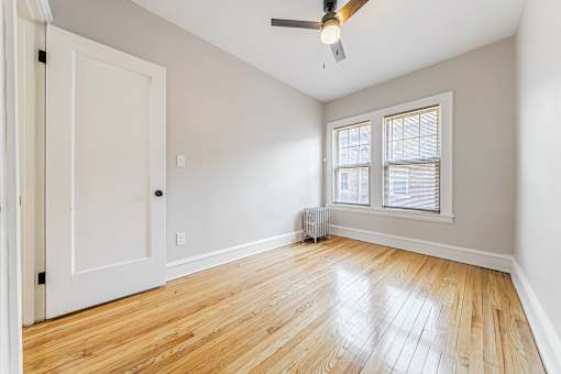A room with a white door, a window with blinds, and a ceiling fan.